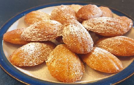 Madeleines dusted with icing sugar on a blue-rimmed plate