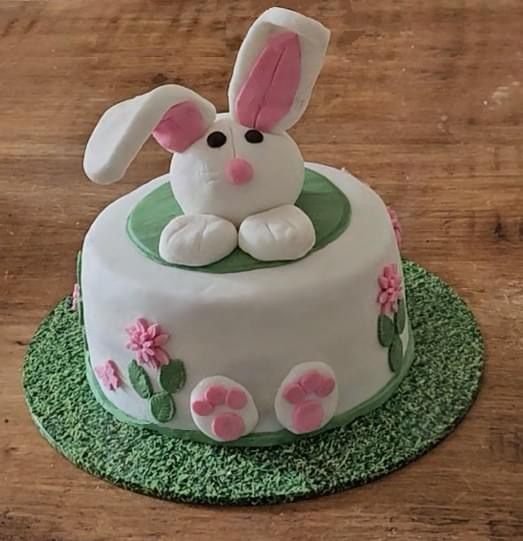 A white cake with a sugar rabbit peeping over the top and flowers round the side