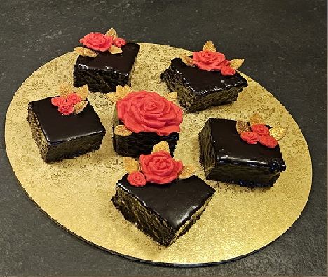 Chocolate-glazed slices topped with red sugar roses, set out on a gold board