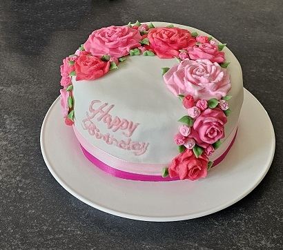 A white iced birthday cake trimmed with pink sugar roses